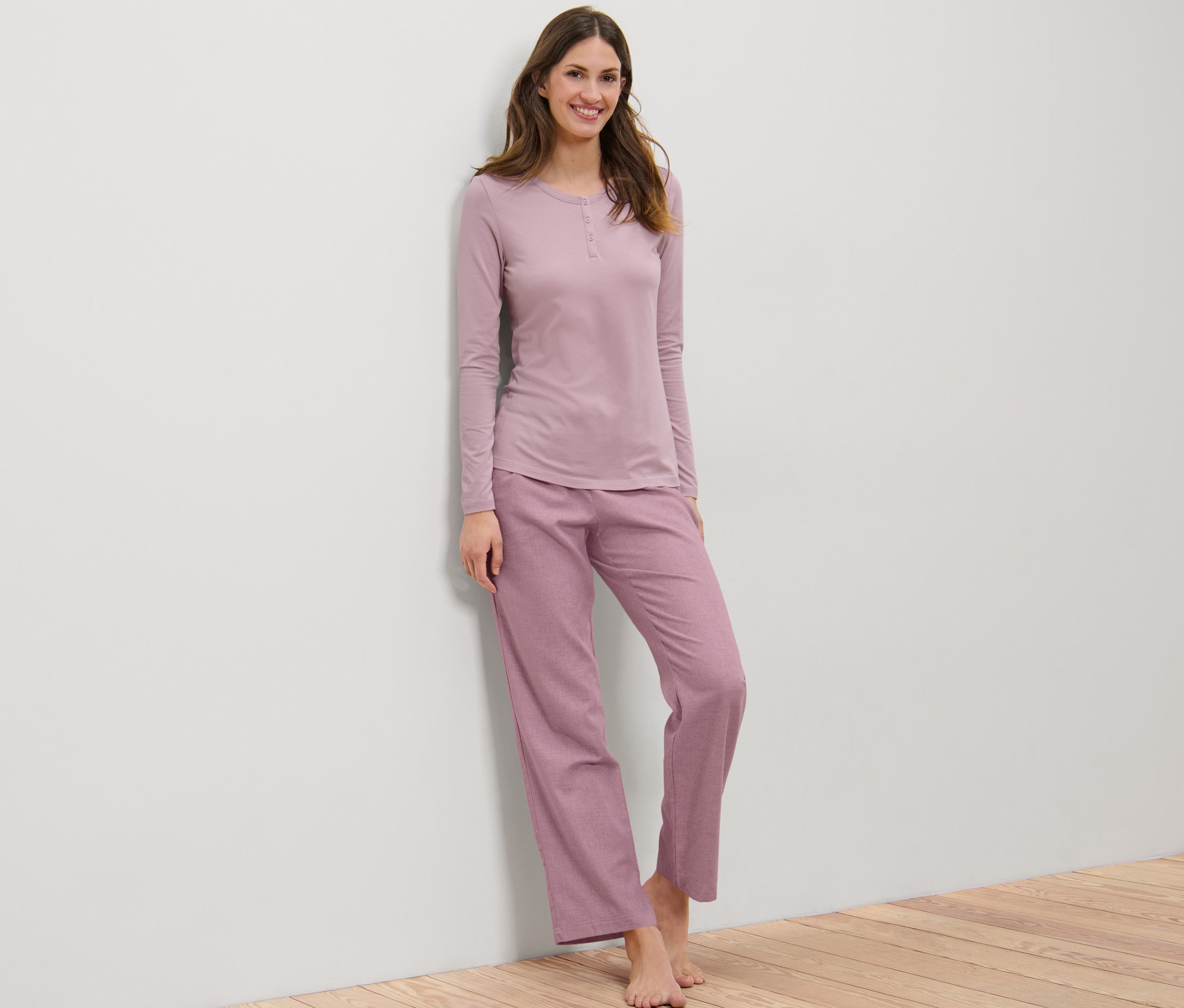 Žena opřená o zeď má na sobě flanelové pyžamo.