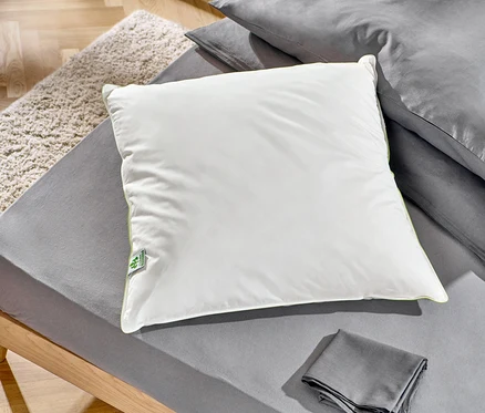 Na posteli leží dva péřové polštáře irisette® greenline: jeden cca 90 x 70 cm a druhý cca 80 x 80 cm.