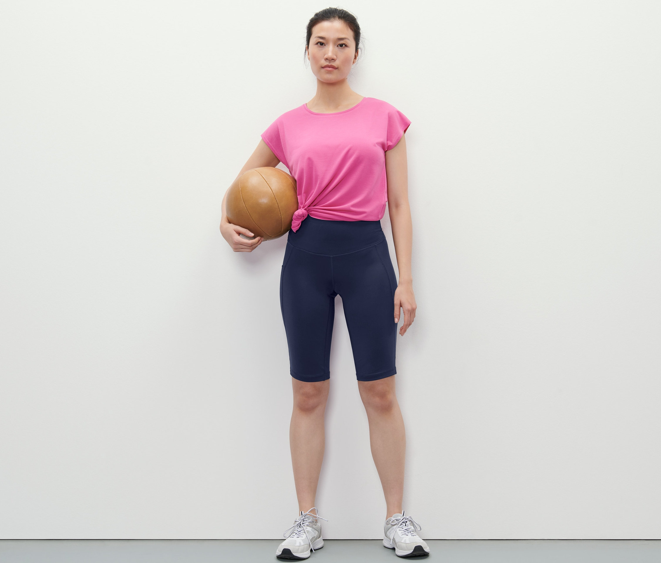 Žena drží basketbalový míč a má na sobě tmavě modré sportovní cyklistické šortky.