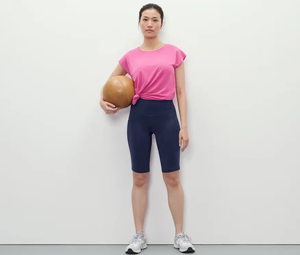 Žena drží basketbalový míč a má na sobě tmavě modré sportovní cyklistické šortky.