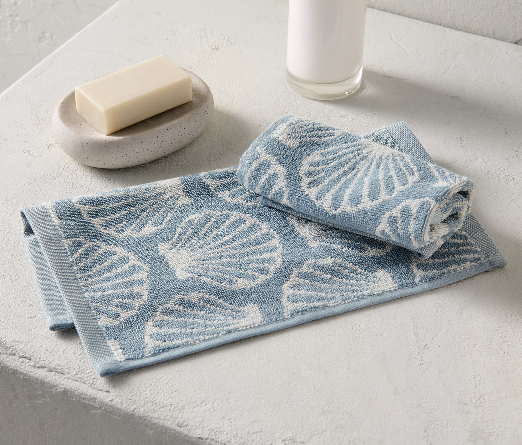 Dvě žínky s potiskem mušlí leží vedle mýdla a dávkovače mýdla.