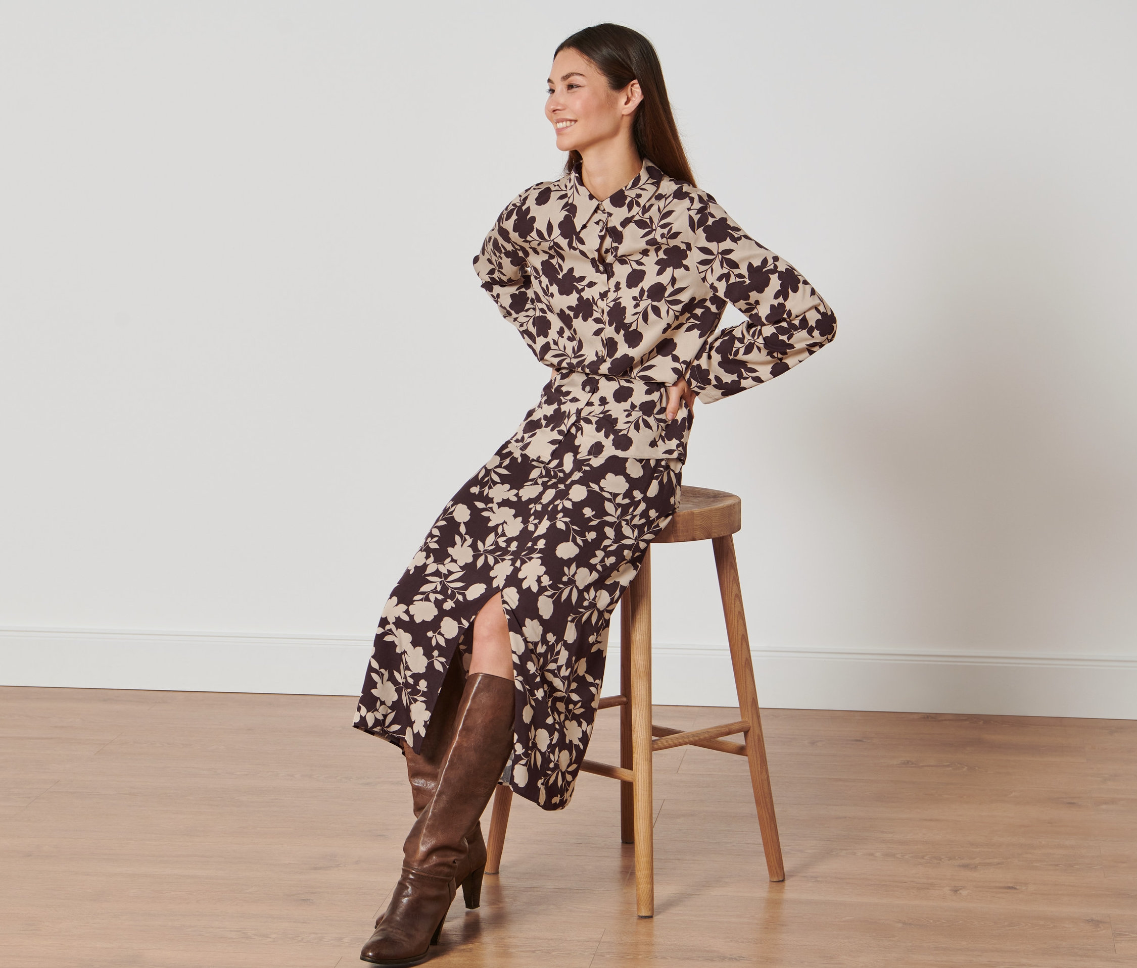 Žena sedí na stoličce a má na sobě sukni s celopotiskem.