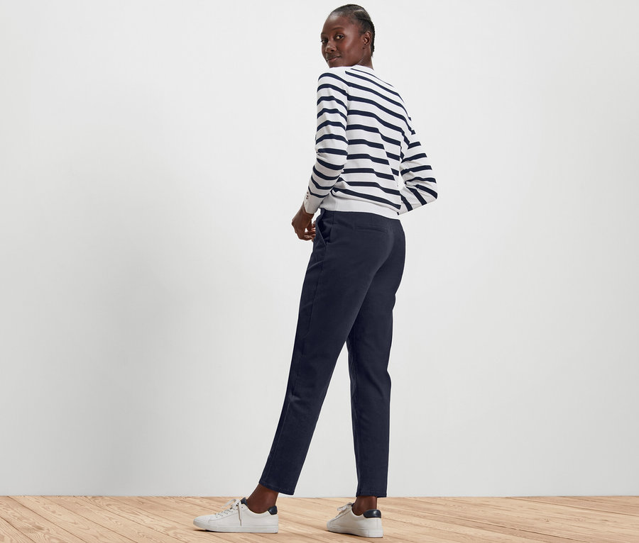 Žena pózuje v tmavě modrých chino kalhotách a pruhovaném svetru.