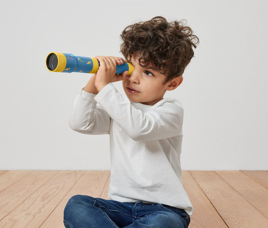 Chlapec sedí na podlaze a dívá se skrz dětský dalekohled.