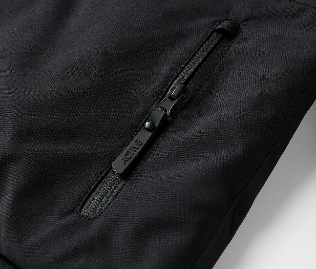 Detail černého zipu na bundě s nápisem ACTIVE.
