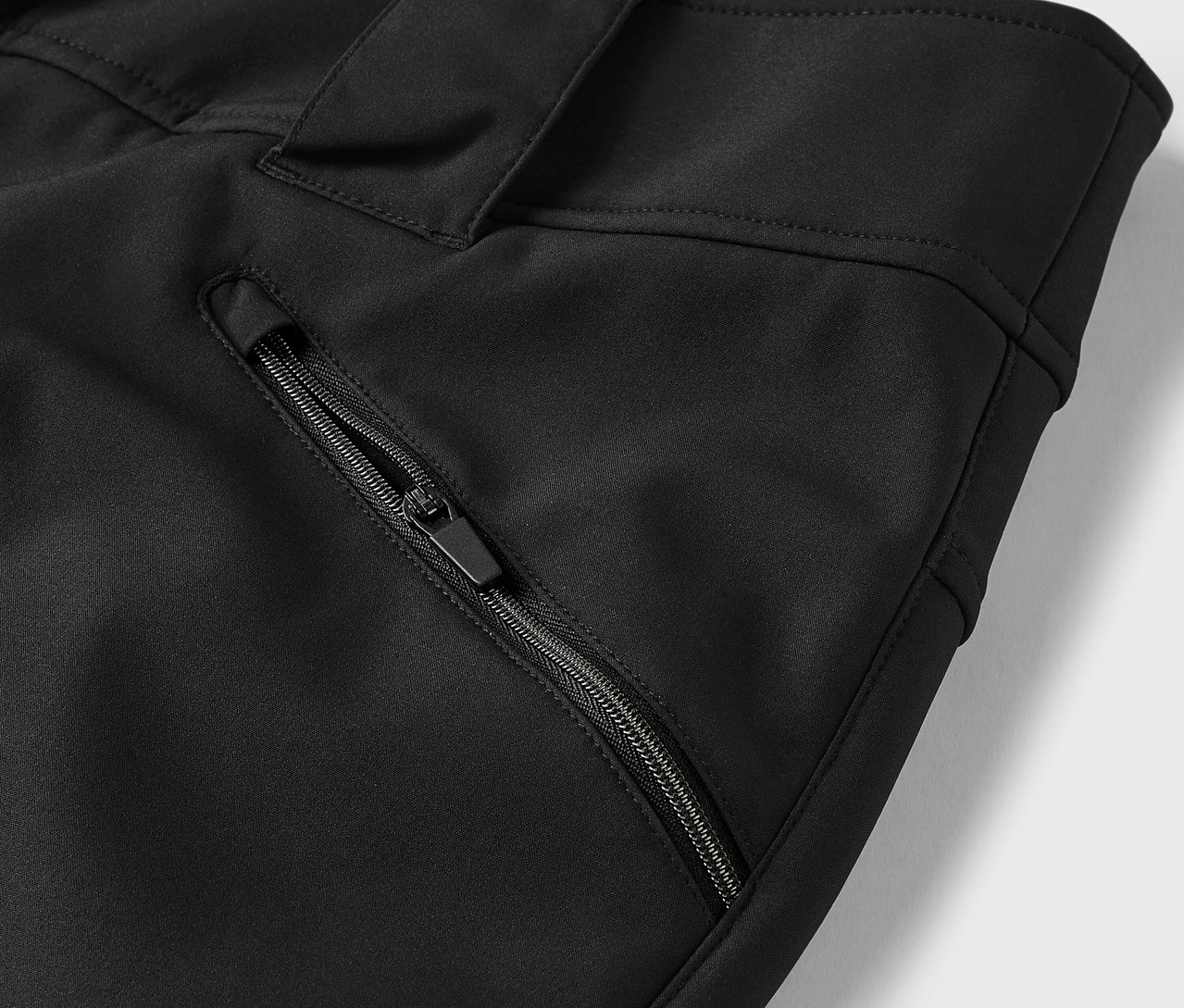 Detail černých kalhot s kapsou na zip.