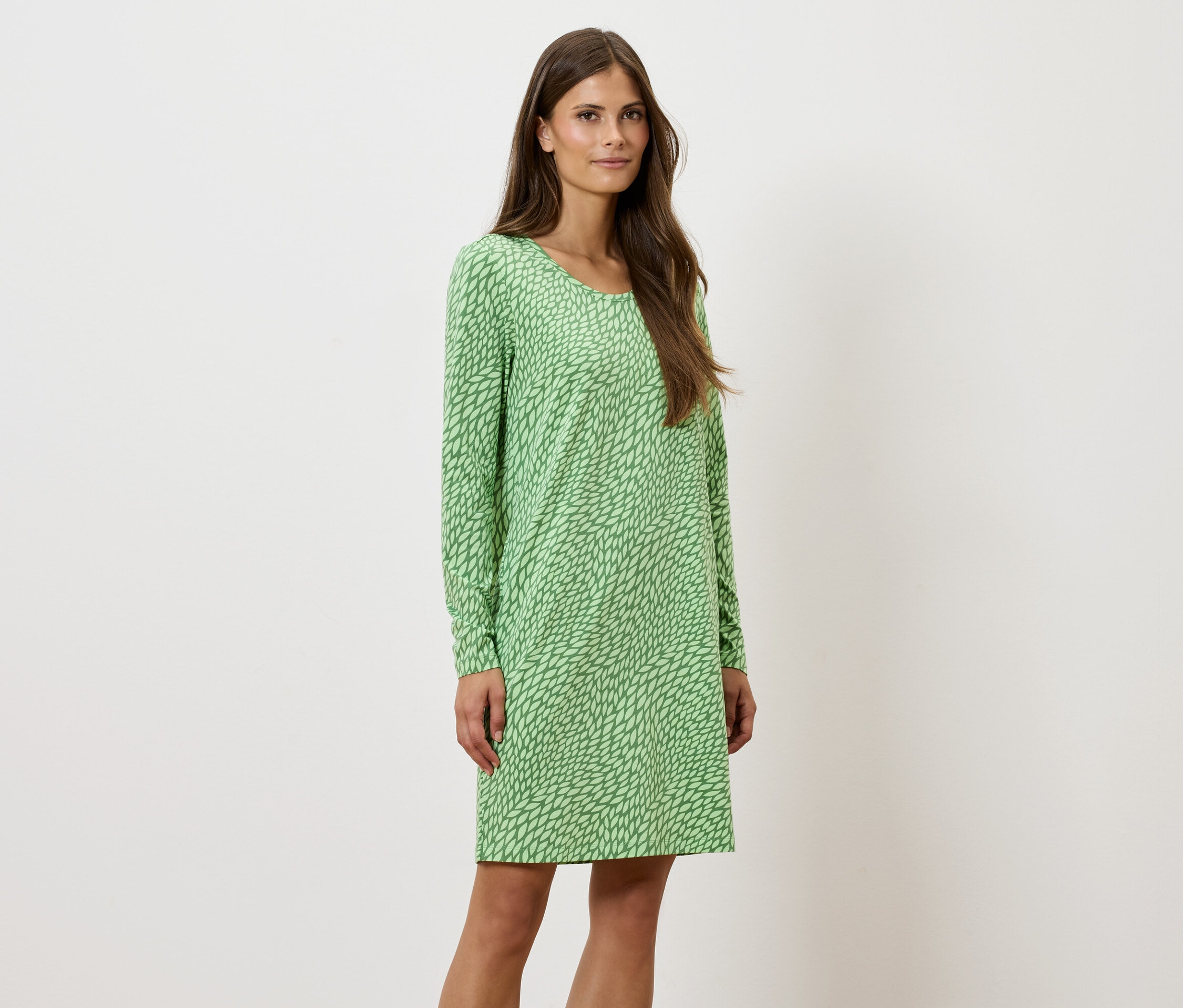 Žena stojí a pózuje v zelených vzorovaných šatech s dlouhým rukávem.