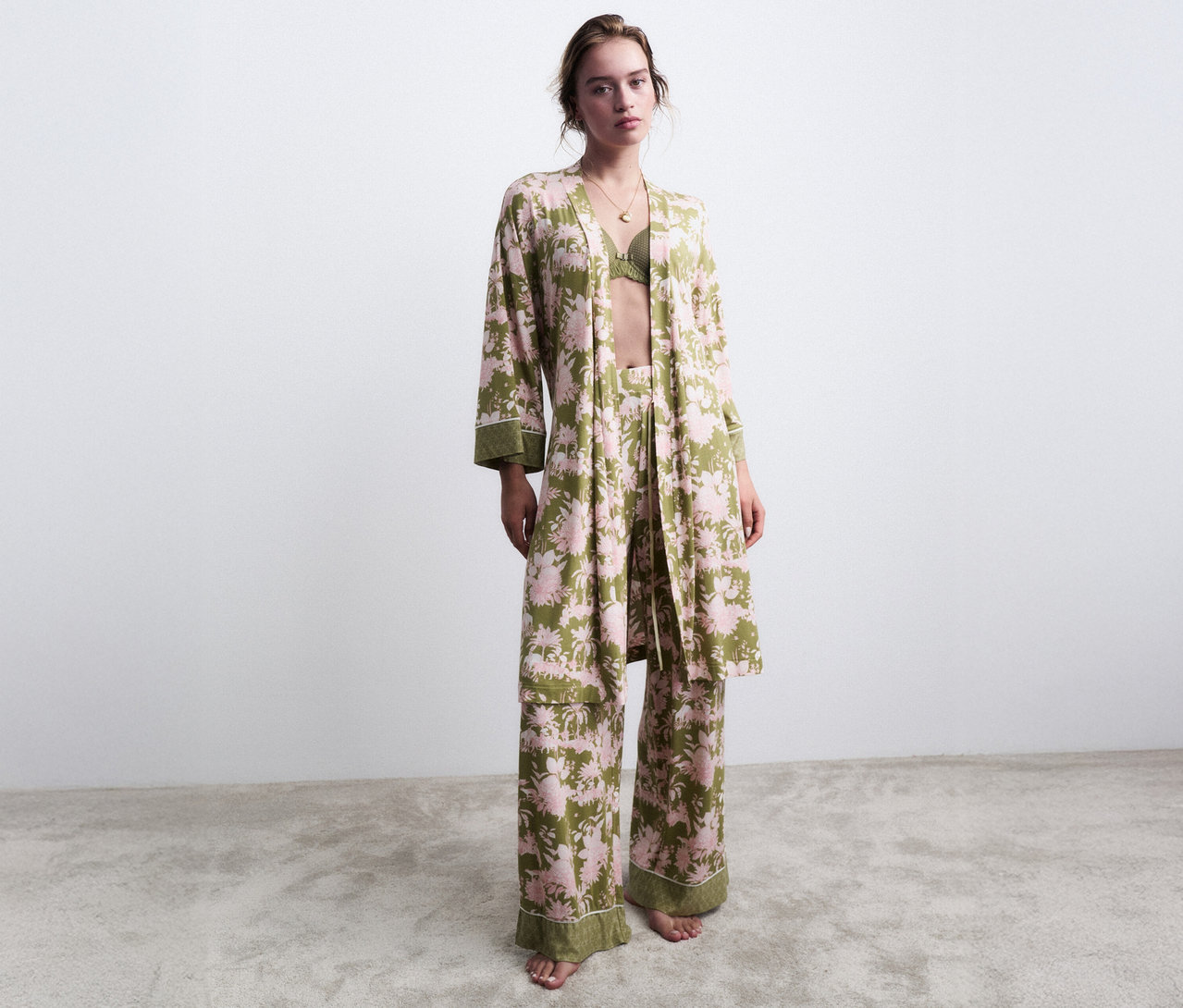 Žena stojí bosá v zeleném květinovém pyžamu s odpovídajícím županem.
