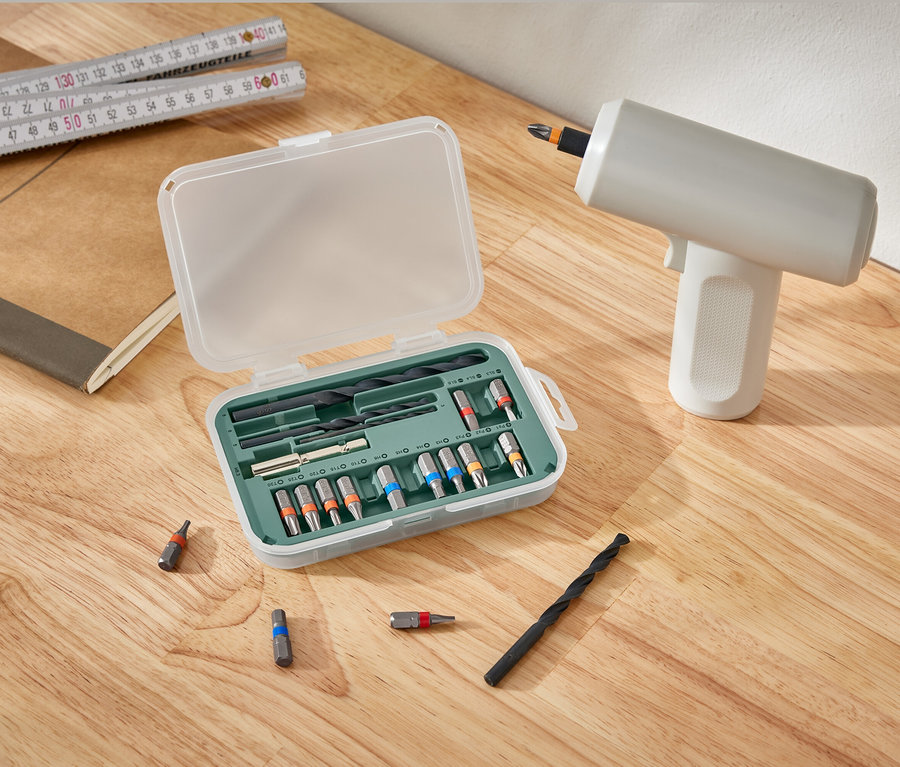 Sada pro šroubovací a vrtací stroje leží otevřená vedle vrtačky na dřevěném stole.