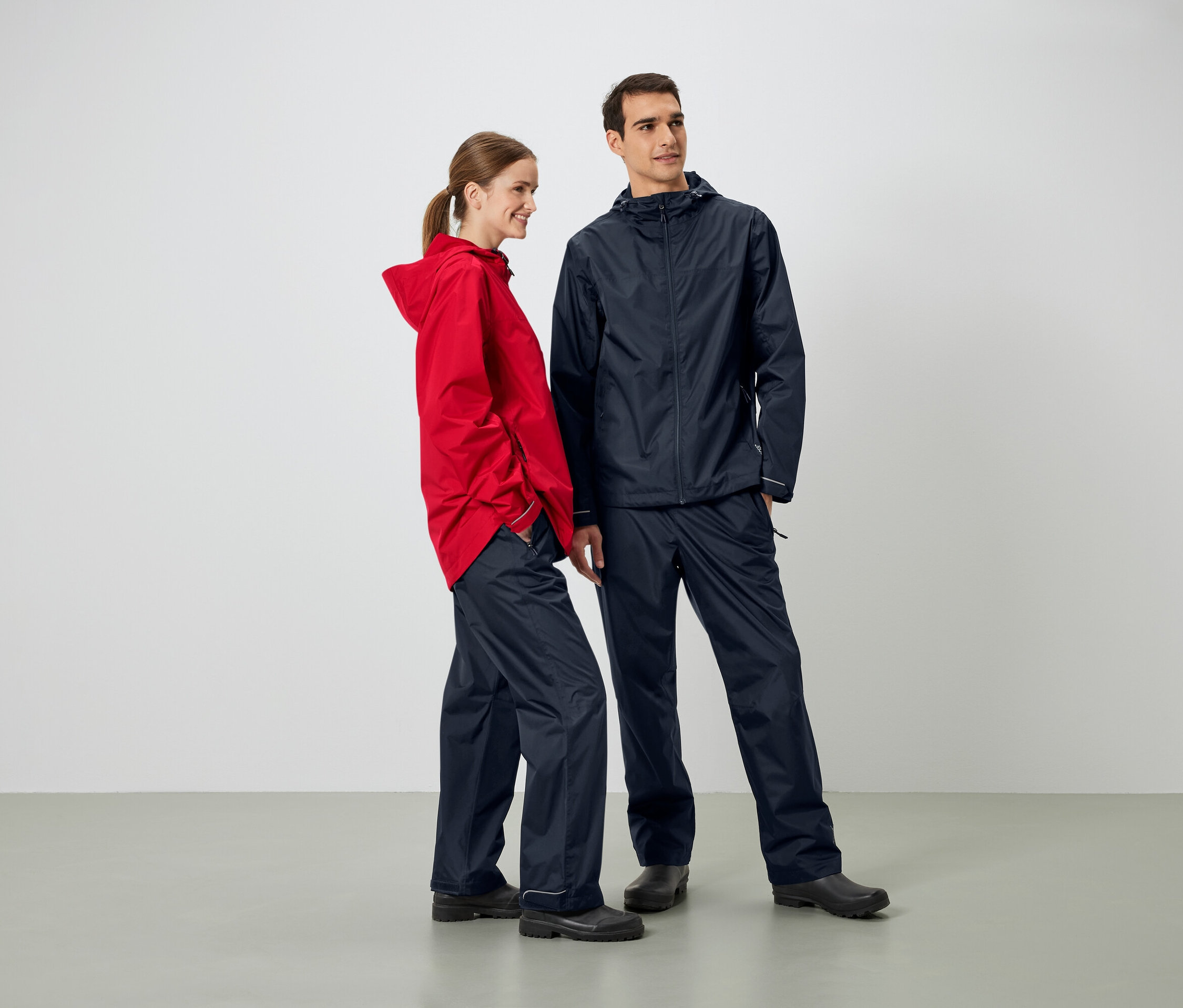 Muž a žena stojí vedle sebe a mají na sobě bundy a kalhoty do deště.