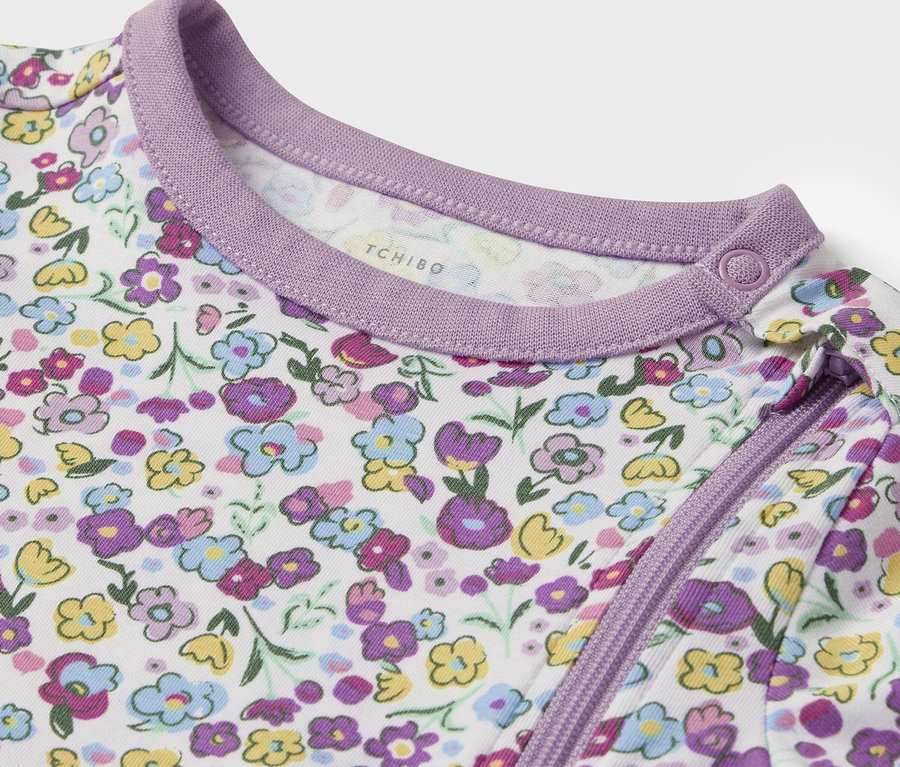 Detail bílého kojeneckého oblečení s fialovými a žlutými květy a fialovým lemem.