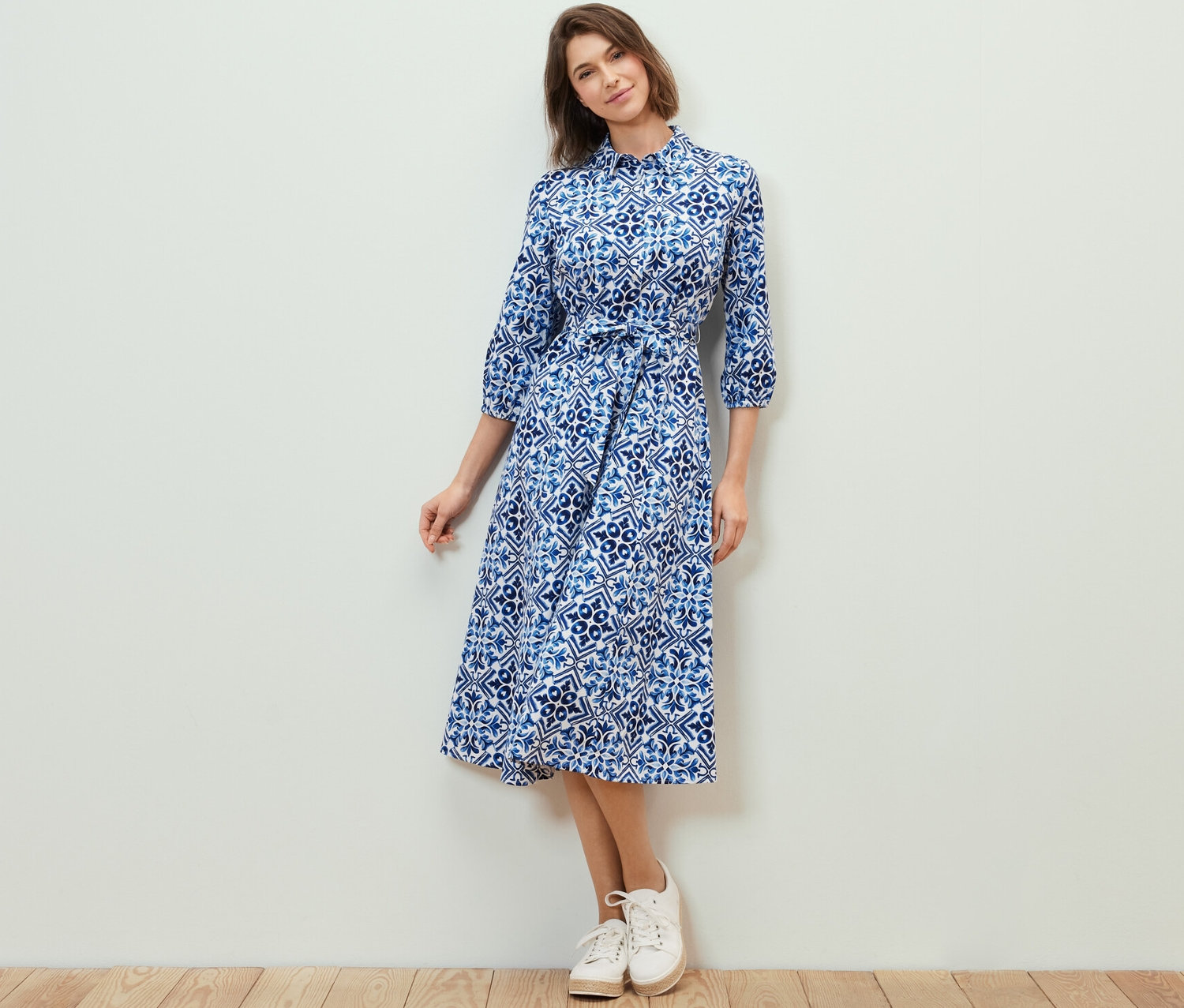 Žena pózuje v midi šatech s potiskem.