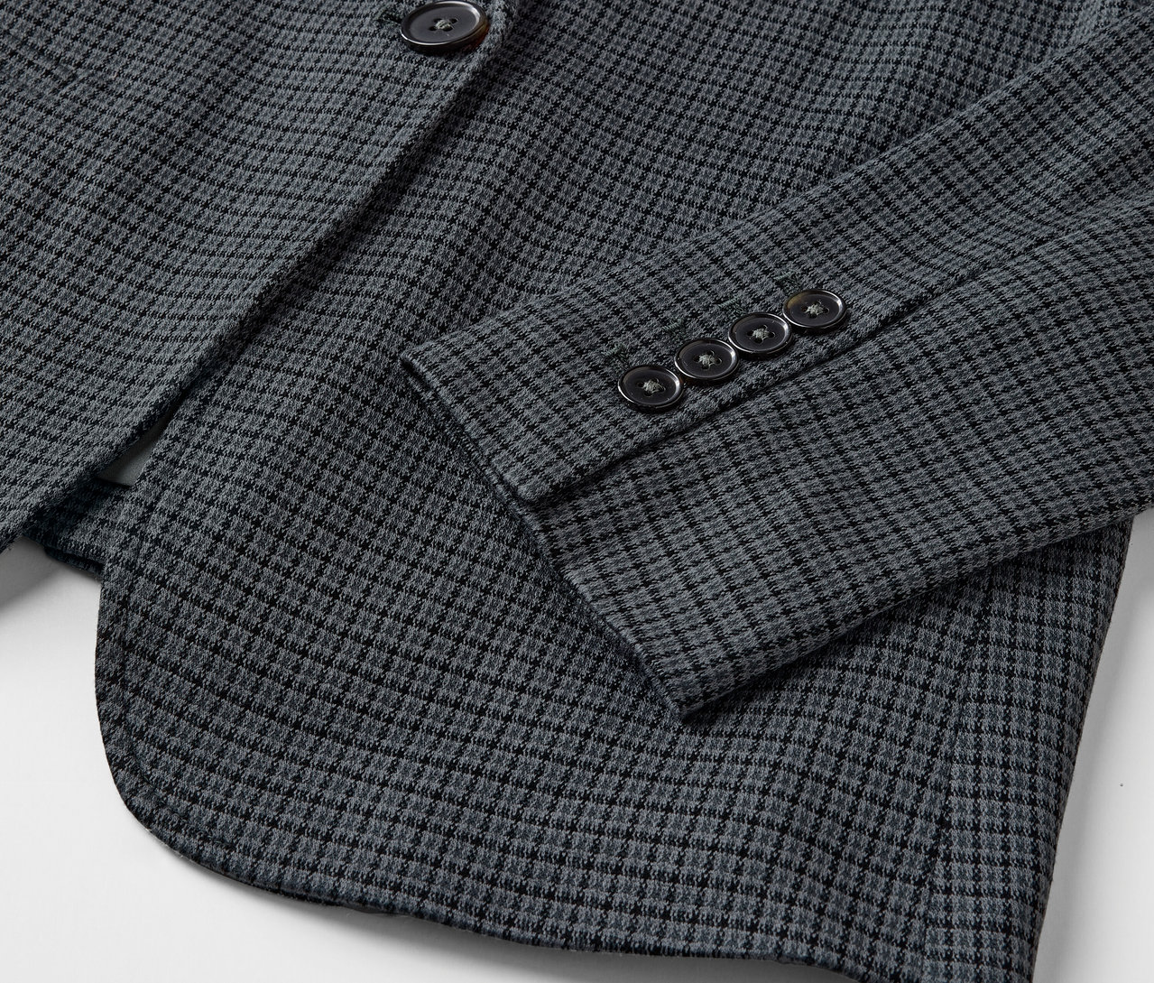 Detail šedého blejzru s drobným vzorem a knoflíky na rukávu.