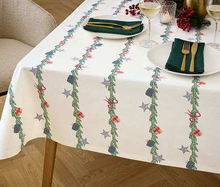 Detail stolu s vánočním ubrusem, na kterém jsou talíře, příbory a sklenice.