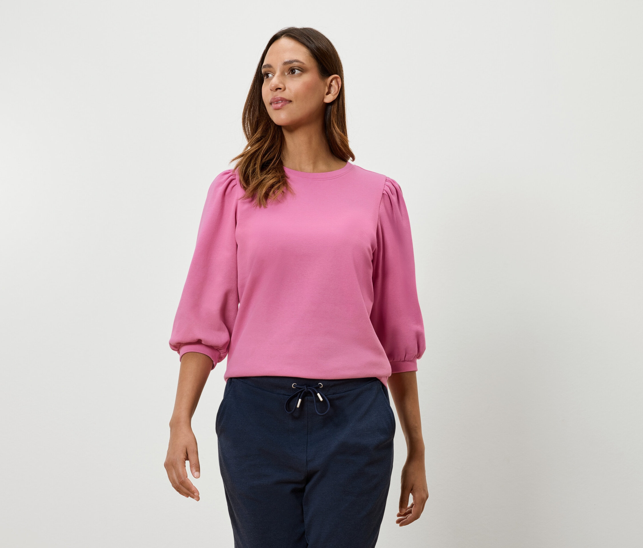 Žena má na sobě růžovou mikinu s tříčtvrtečními balónovými rukávy a tmavě modré kalhoty.