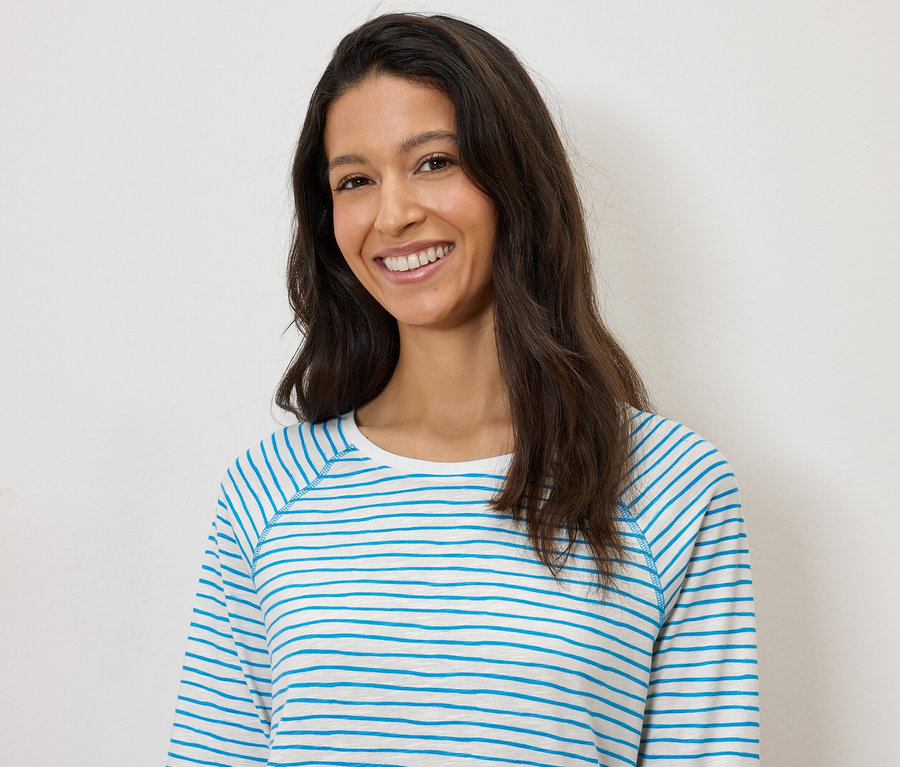 Usmívající se žena v modro-bílém pruhovaném tričku s dlouhým rukávem na bílém pozadí.