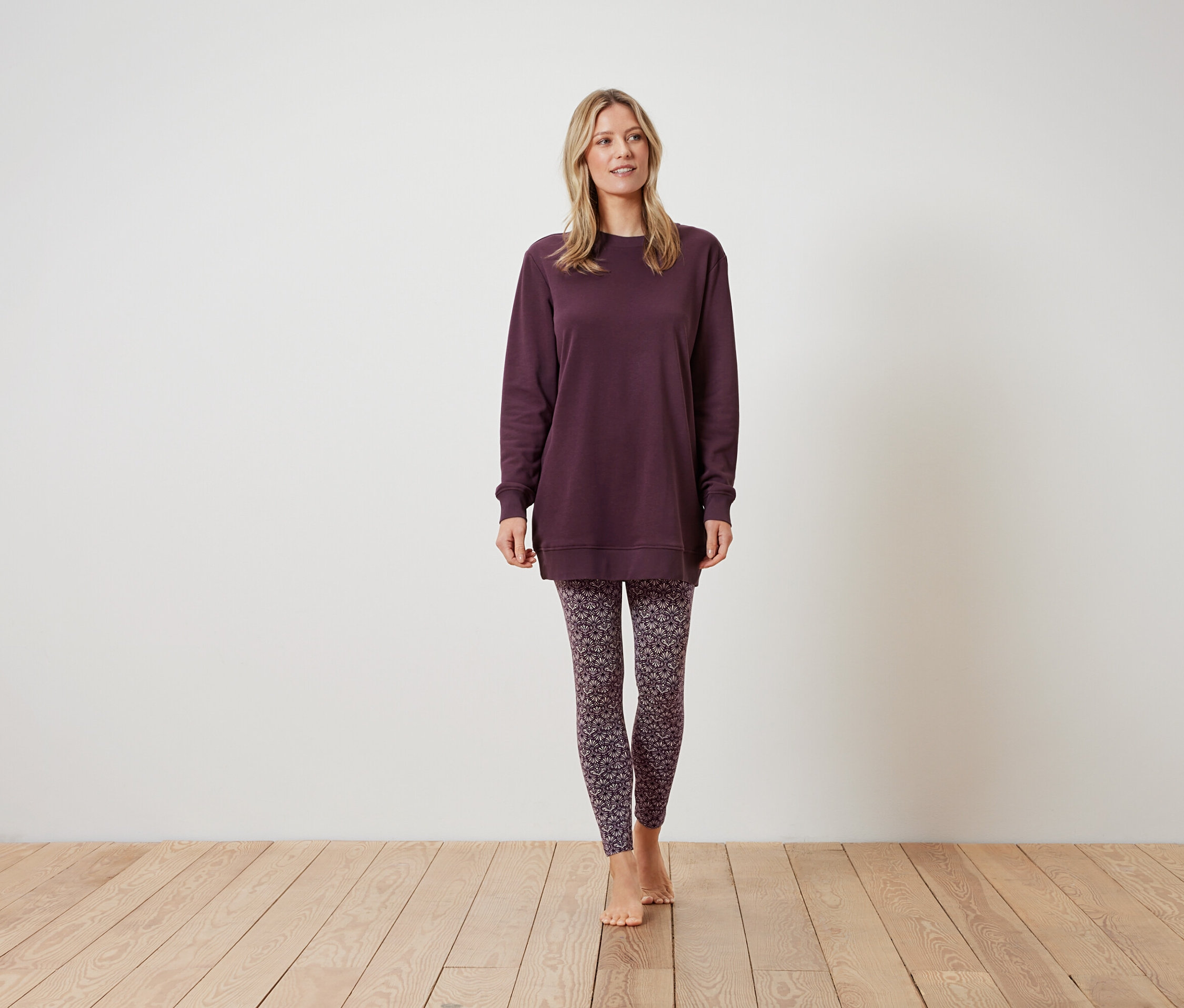Žena stojí a má na sobě vínovou mikinu a vzorované legíny.