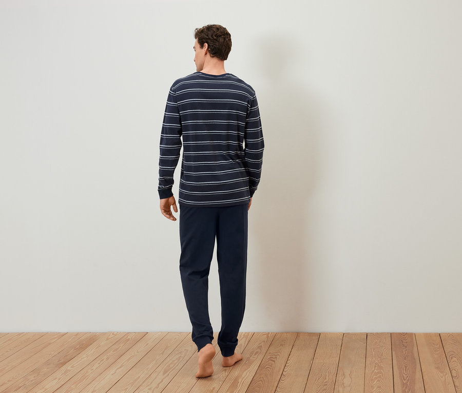 Muž v pruhovaném pyžamu jde bosý po dřevěné podlaze.