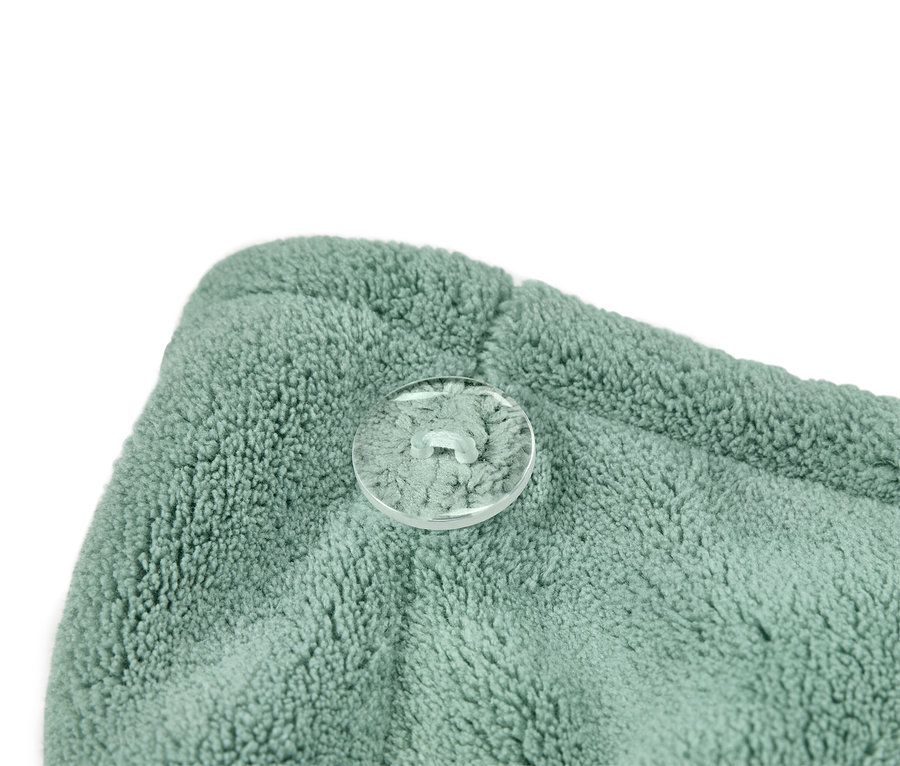 Detailní záběr na tyrkysově zelený turban na ručník s průhledným knoflíkem.