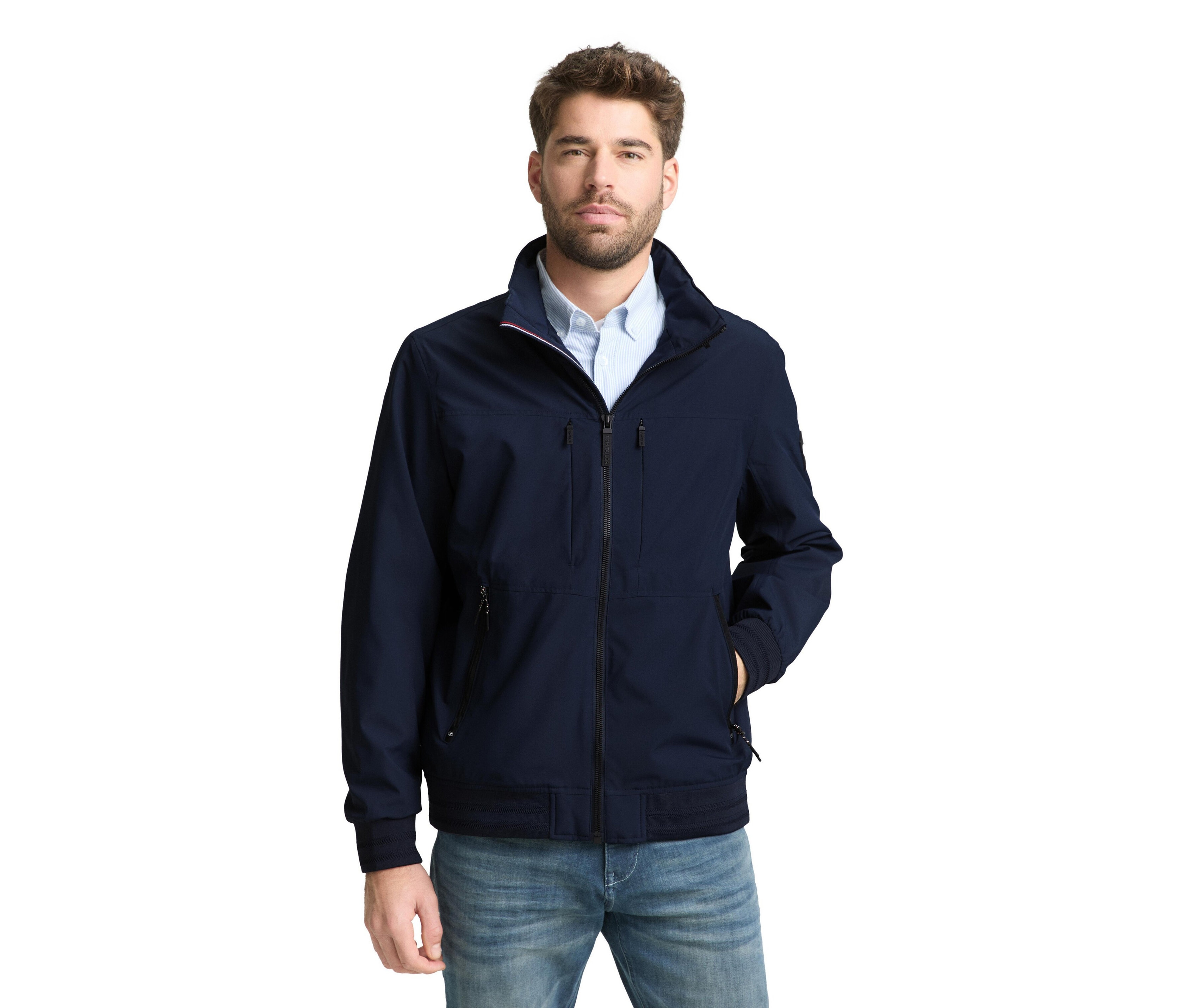 Muž s vousy má na sobě tmavě modrou bundu a džíny.