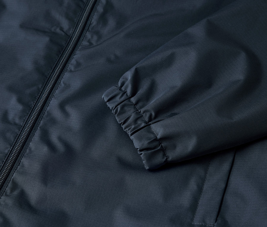 Detailní pohled na tmavě modrou bundu se zipem a elastickými manžetami.