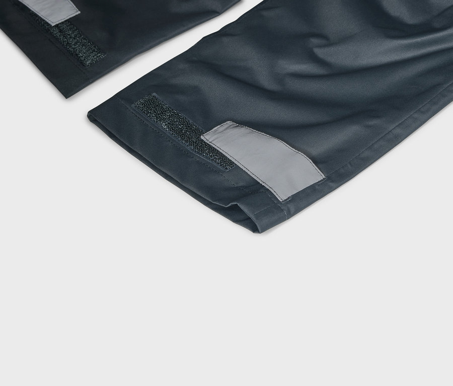 Detailní pohled na tmavě modré nohavice se suchým zipem a reflexními detaily na lemech.