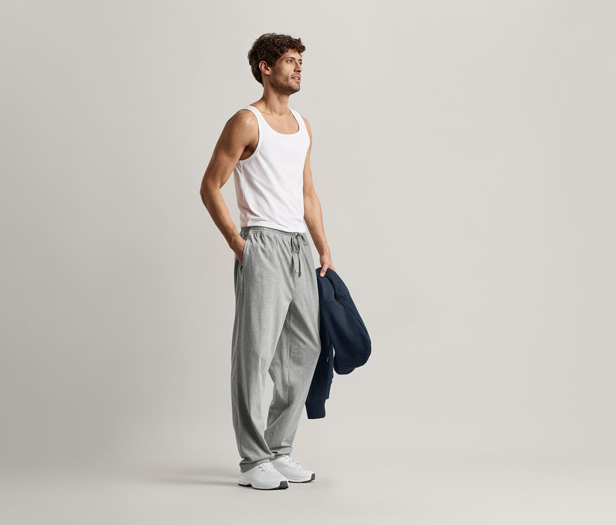 Muž v bílém tílku a šedých pohodlných kalhotách.