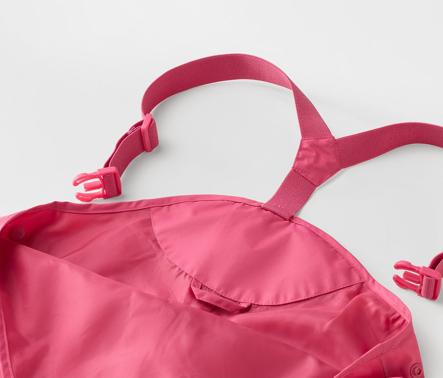 Detail růžových dětských nepromokavých kalhot s nastavitelnými ramínky a přezkami na bílém pozadí.
