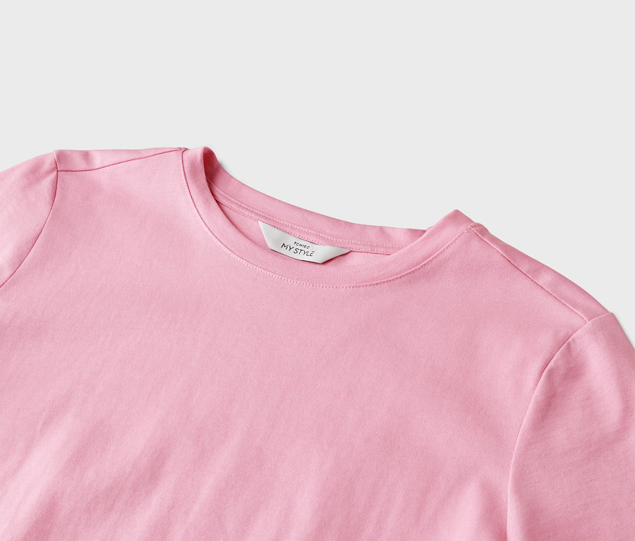 Detailní záběr na světle růžové tričko s kulatým výstřihem a bílým štítkem s nápisem „Tchibo My Style“.