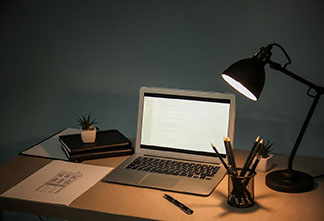 Správné místo pro světlo: Černá kancelářská lampa stojí na dřevěném psacím stole vedle notebooku.