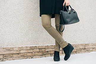 Mladá elegantní žena v hravé bílé krajkové halence a elegantních světle hnědých kalhotách culottes sedí u růžově natřené cihlové zdi a telefonuje svým smartphonem.