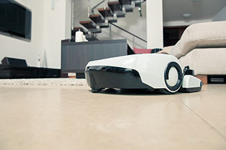 Električtí pomocníci: Robotický vysavač jede po podlaze s dlažbou v obývacím pokoji.