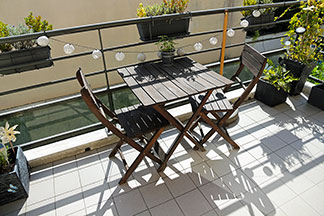 Zahradní židle na balkon: Na malém balkonu stojí dvě dřevěné židle a čtvercový dřevěný stůl.