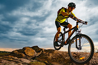 Mladý muž, který má na sobě cyklistický dres s krátkým rukávem a cyklistické šortky, jede na horském kole na horách.