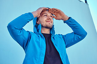 Bunda na přechodné období: Mladý muž v modré softshellové bundě má ruce na čele a dívá se do dálky.