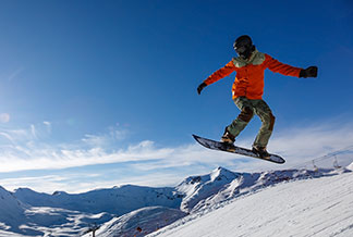 Pánské sportovní bundy na zimu: Snowboardista skáče v zasněžených horách.