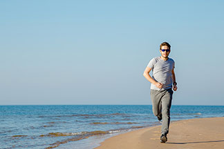 Mladý muž běží v klasických šedých joggingových kalhotách podél pláže.